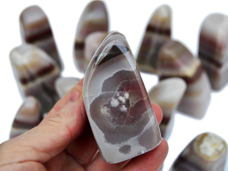 One pink banded onyx free form 60mm on hand with background with some stones on white