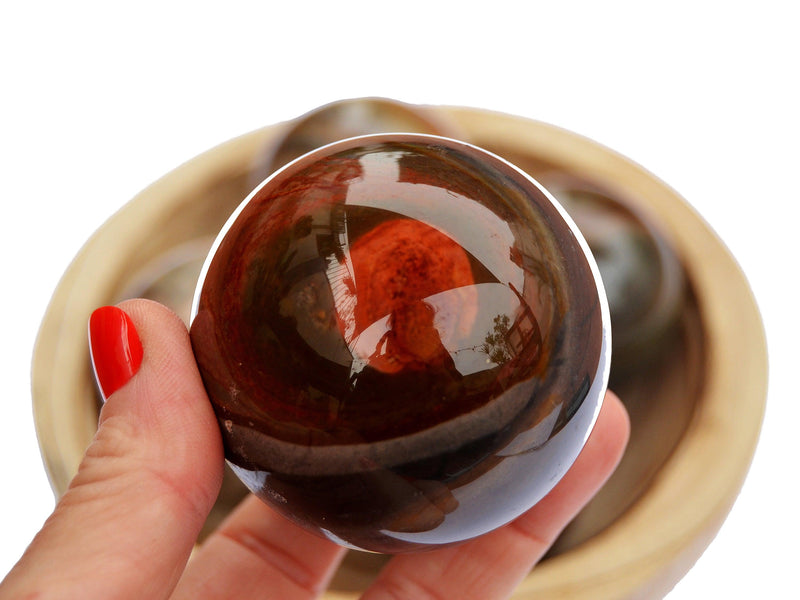 One multicolor polychrome jasper sphere 55mm on hand with background with some spheres inside a wood bowl