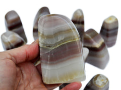 One large pink banded onyx free form mineral 110mm on hand with background with some stones on white