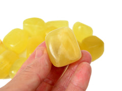 One lemon calcite cube tumbled stone on hand with background with some crystaks on white