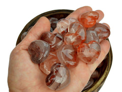 Ten fire quartz heart crystals 30mm on hand with background with some stones inside a wood bowl