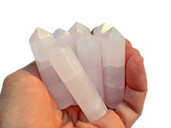 Some pink mangano calcite faceted crystal points on hand with background with some points on white background