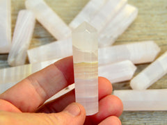 One pink mangano calcite crystal point 55mm on hand with background with some points on wood table