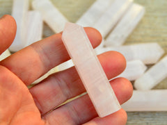 One pink mangano calcite crystal point 60mm on hand with background with some points on wood table