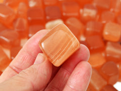 One honey calcite cube tumbled  crystal on hand with background with several crystals