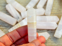 One pink mangano calcite crystal tower 60mm on hand with background with some points on wood table