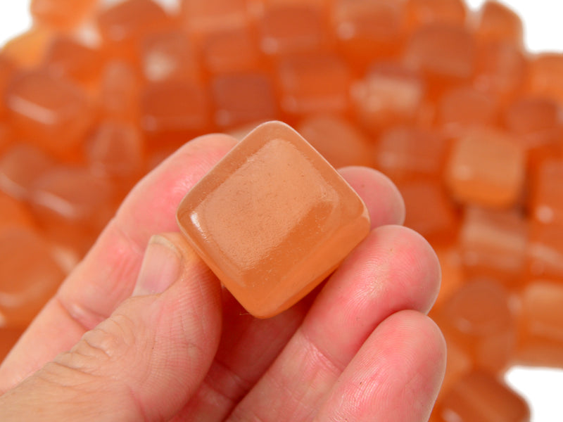 One honey calcite cube tumbled stone on hand with background with several crystals