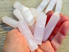 Some pink mangano calcite faceted crystal points on hand with background with some points on wood table