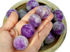 Four purple amethyst sphere stones on hand with background with some crystals inside a wood bowl