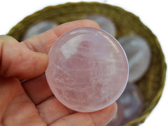 One rose quartz palm stone 50mm on hand with background with some crystals inside a straw basket on white background