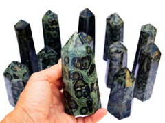 One kambaba jasper tower 100mm on hand with background with several obelisks on white