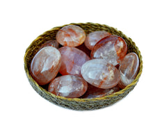 Several hematoid quartz crystal palm stones 40mm-70mm inside a straw basket on white background