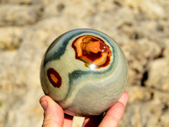 One desert jasper sphere mineral 70mm on hand with natural rock background