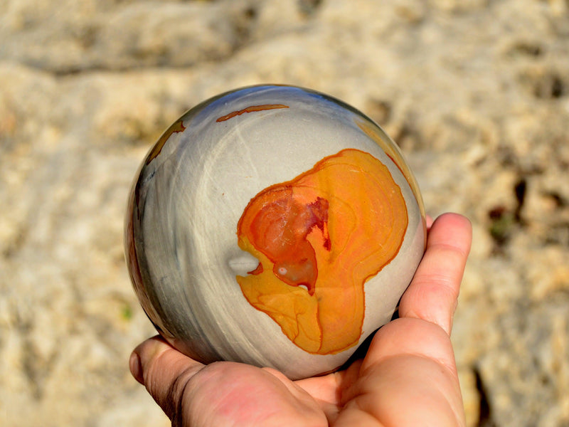 One desert jasper sphere mineral 80mm on hand with natural rock background