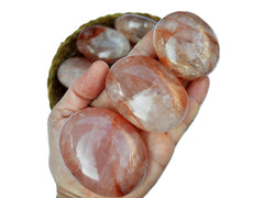 Three fire quartz palm stones 50mm-70mm on hand with background with some gemstones inside a straw basket on white