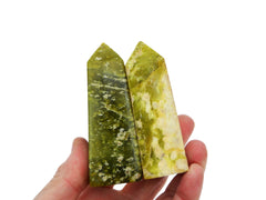 Two green serpentine obelisk crystals 70mm on hand with white background