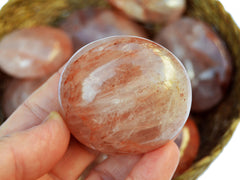 One fire quartz palm stone 60mm on hand with background with some crystals inside a straw basket
