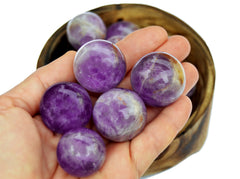 Five purple amethyst sphere stones on hand with background with some crystals inside a wood bowl