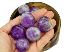 Some amethyst crystal spheres 25mm - 40mm on hand with background with some stone balls inside a bowl