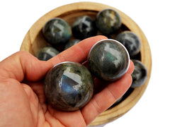Two labradorite sphere stones 25mm-30mm on hand with background with some balls inside a wood bowl