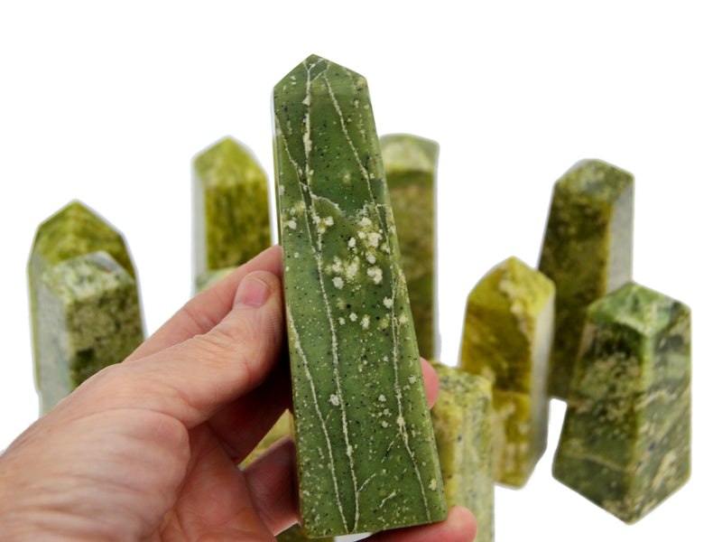 One large green serpentine mineral obelisk on hand with background with some stones on white