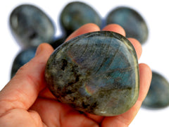One big labradorite palm stone 60mm on hand with background with some crystals