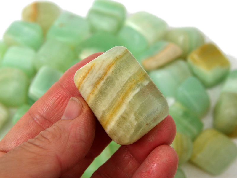 One pistachio calcite tumbled stone on hand with background with several crystals 