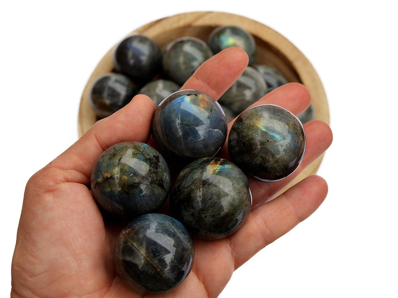 Four labradorite sphere stones 25mm-30mm on hand with background with some balls inside a wood bowl