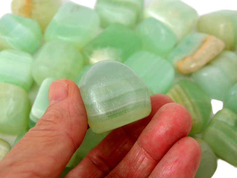 One pistachio calcite cube tumbled stone on hand with background with several crystals 