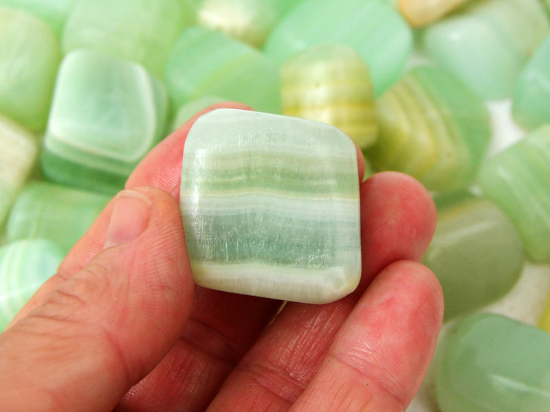 One pistachio calcite tumbled stone on hand with background with some crystals