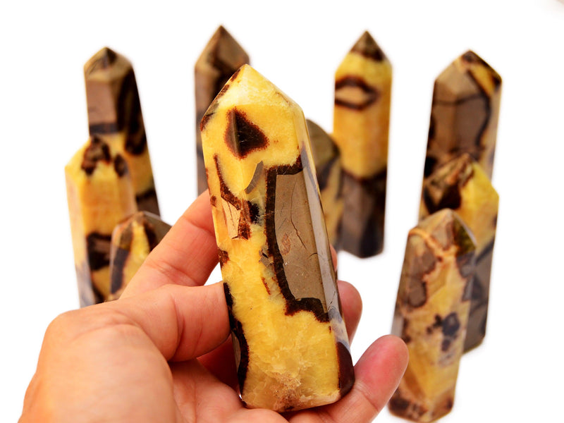 One yellow septarian crystal obelisk 95mm on hand with background with some towers on white
