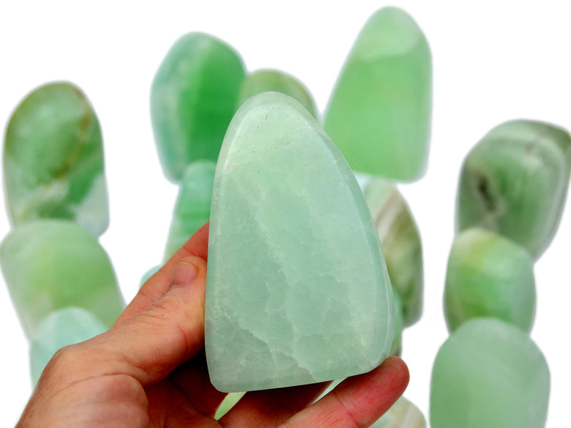 One pistachio calcite free form 70mm on hand with background with some crystals on white