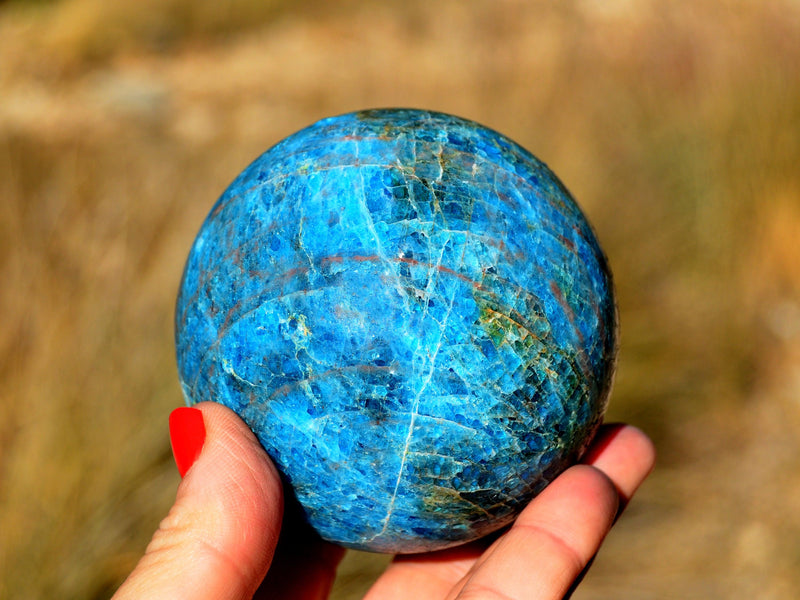 One large blue apatite sphere 70mm on hand with straw background