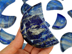 One large blue lapis lazuli crystal moon on hand with background with some lapis moons on white