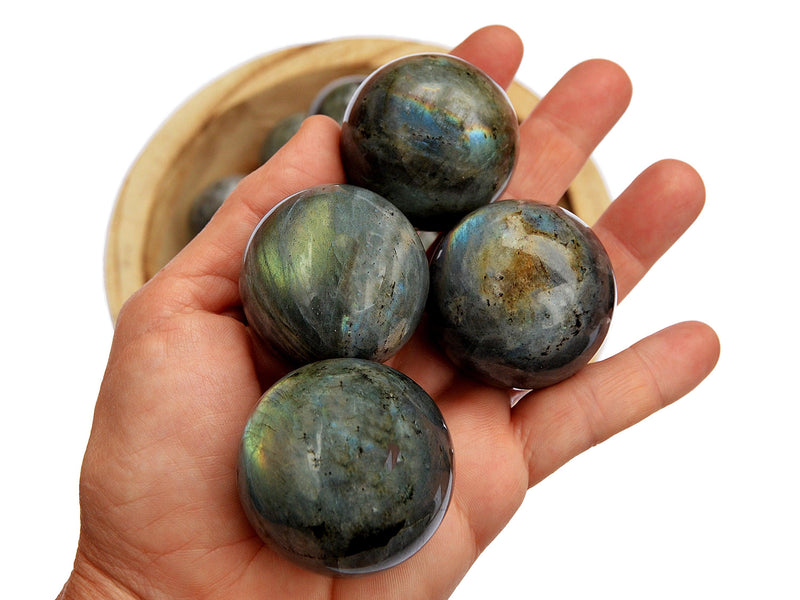 Five labradorite spheres 35mm-40mm on hand with background with some crystals inside a wood bowl