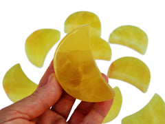 One lemon calcite moon stones 65mm on hand with background with some yellow calcite moons on white
