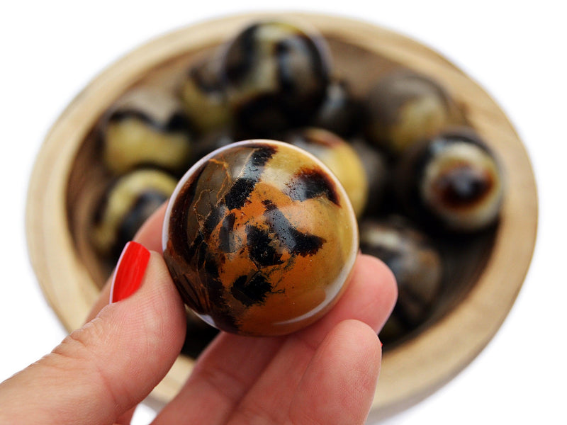 One yellow septarian crystal sphere 30mm on hand with background with some spheres inside a wood bowl