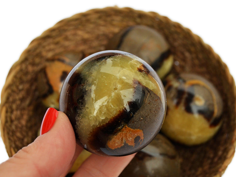 One yellow septarian sphere crystal 45mm on hand with  background with some spheres inside a straw basket on white