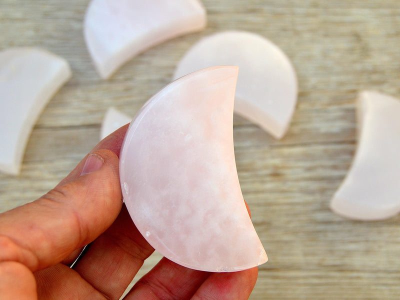 One pink mangano calcite moon crystal 60mm on hand with background with some moons on wood table