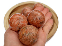 Three natural orange calcite crystal spheres 35mm-40mm with background with some crystals inside a bowl