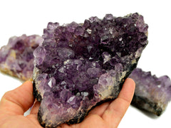 Hand holding a large purple druzy amethyst against a background with some crystals