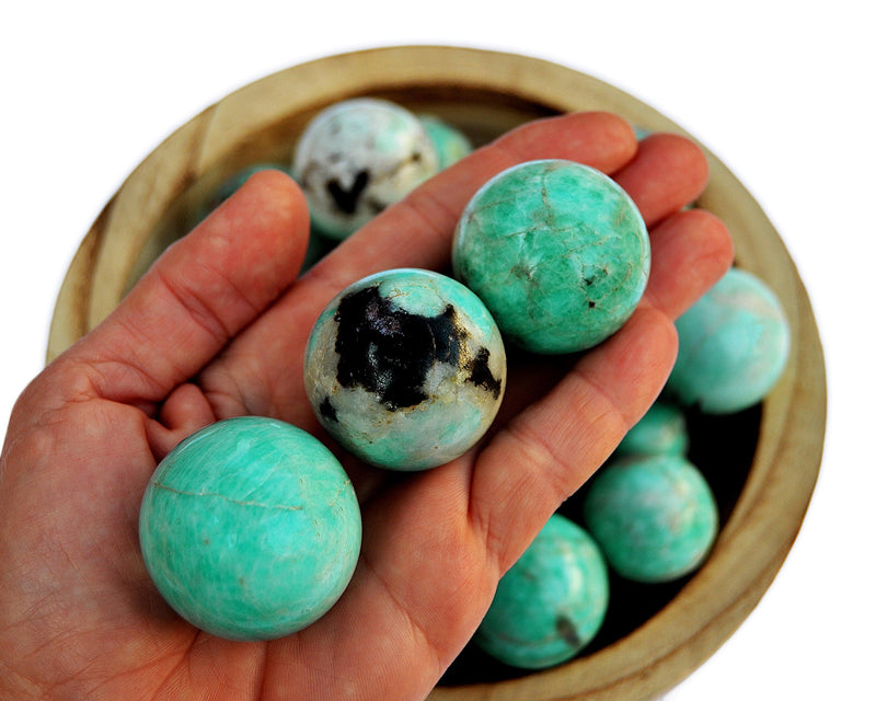 Three amazonite sphere stones 25mm-35mm on hand with  background with some crystals inside a wood bowl