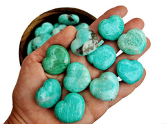 Some small green amazonite puffy hearts 30mm on hand with background with several stones inside a wood bowl