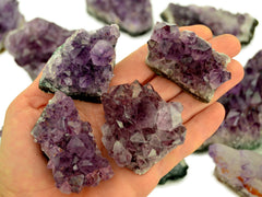 Four amethyst druzy crystals 50mm-60mm on hand with background with some stones on white