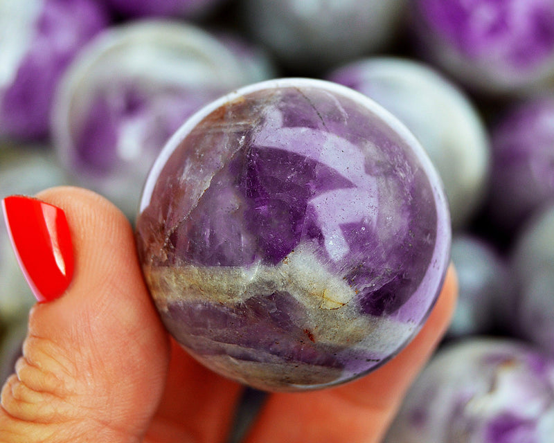 One amethyst crystal sphere 45mm on hand with background with several crystals