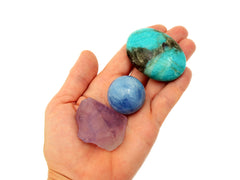 Raw amethyst, blue calcite sphere and amazonite palm stone on hand with white background