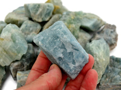 One aquamarine raw crystal 90mm on hand with background with some stones on white