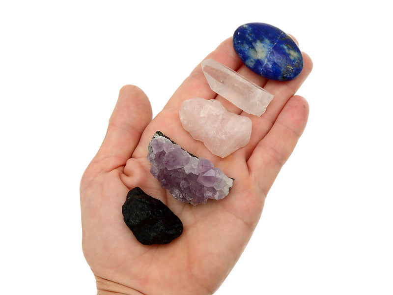 Raw black tourmaline, druzy amethyst, raw rose quartz, clear quartz point and lapis lazuli palm stone on hand with white background