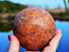 Large orange calcite crystal sphere 95mm on hand with river landscape background
