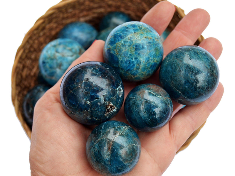Five blue calcite sphere crystals 25mm - 40mm on hand with background with some stones inside a basket